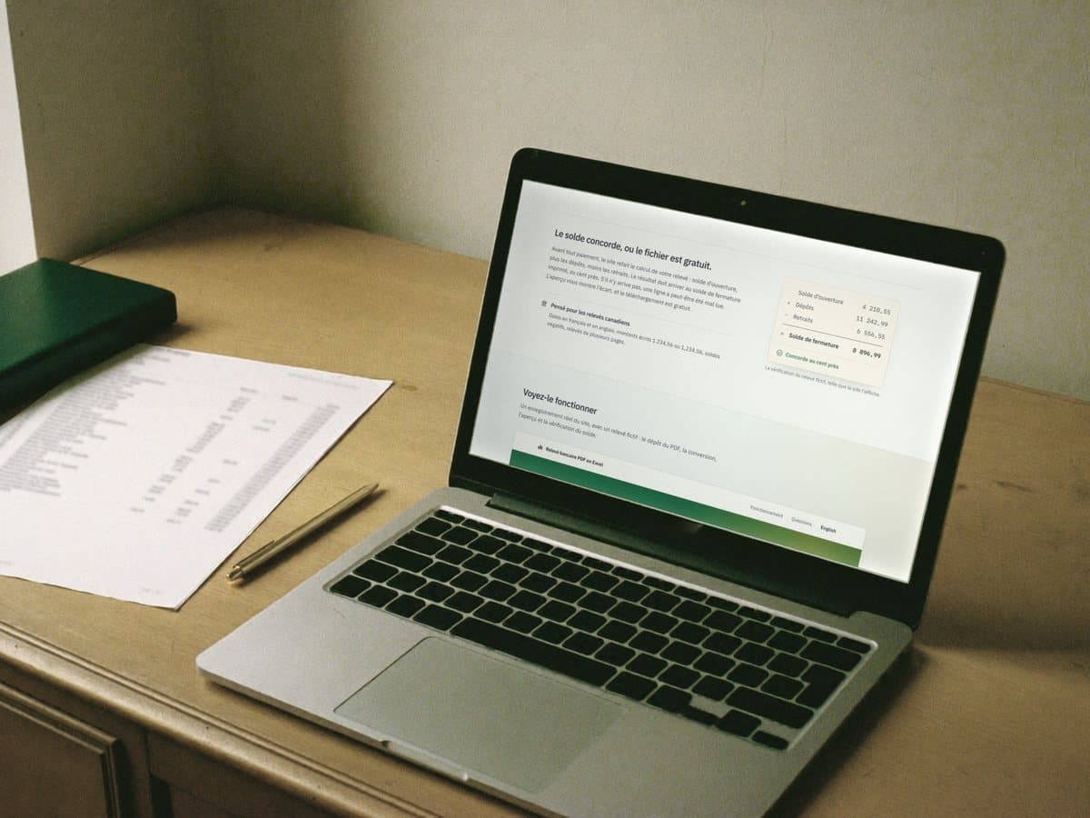 A printed bank statement on an oak desk, beside a laptop showing the balance check for that statement.