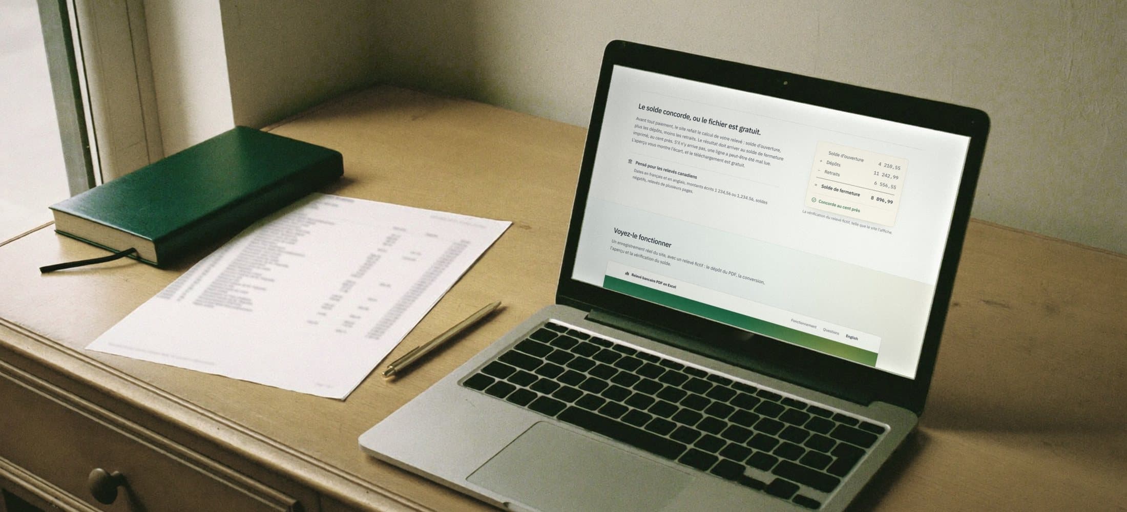 A printed bank statement on an oak desk, beside a laptop showing the balance check for that statement.